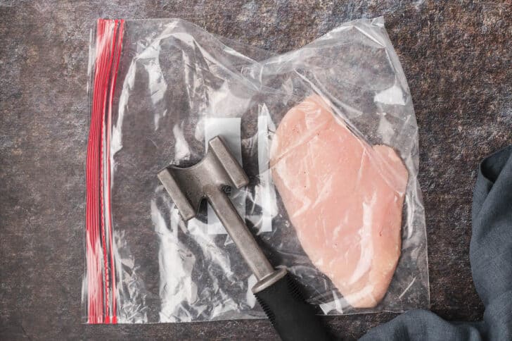 A piece of chicken breast in a ziploc bag, with a meat mallet ready to pound it out.