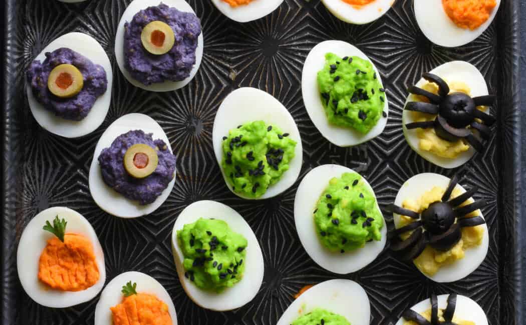 Cookie sheet with various types of Halloween deviled eggs arranged on top.