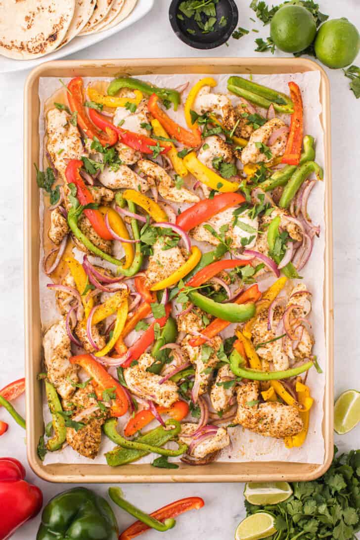 A rimmed baking pan full of cooked poultry, bell peppers and onions garnished with cilantro.