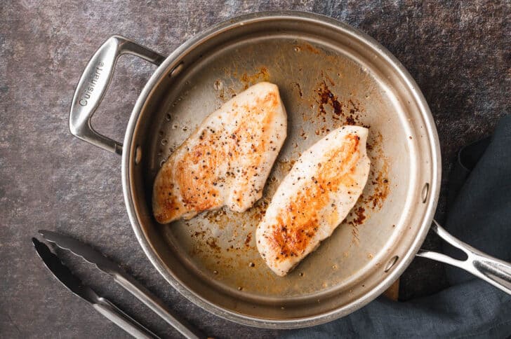 Two chicken breasts being seared in a skillet.