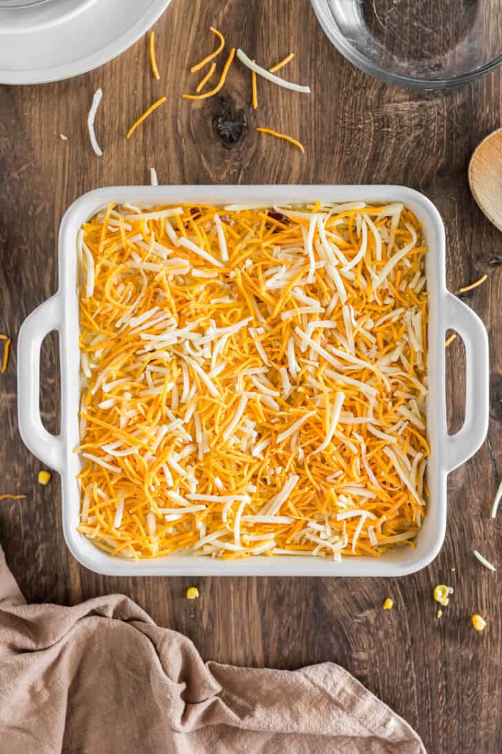 A square white baking dish filled with a cheesy corn recipe, before baking.