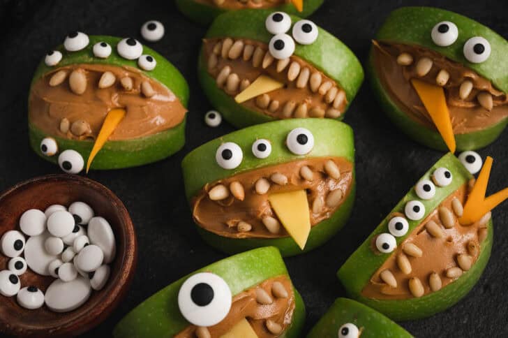 Green apples cut into face shapes and filled with peanut butter and pine nuts so they can be Halloween foods for a party.
