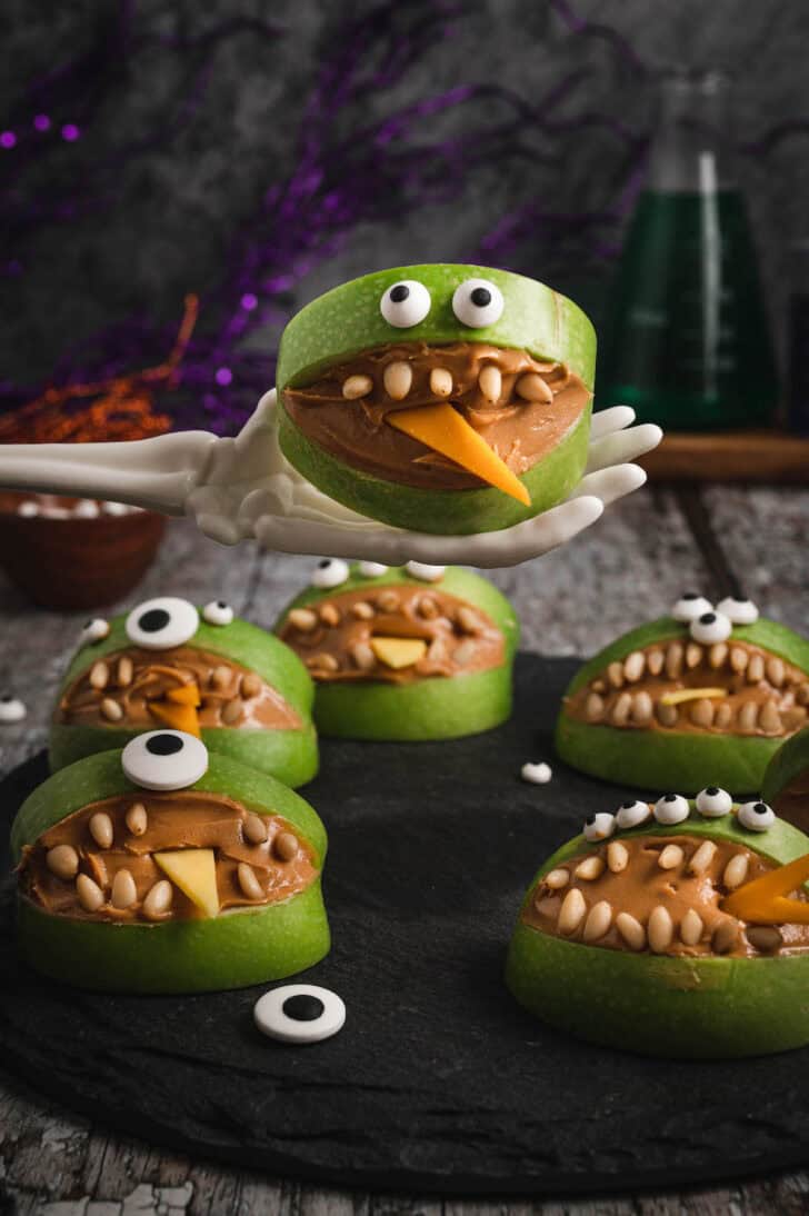 Green apples cut into face shapes and filled with peanut butter and pine nuts so they can be Halloween foods ideas.