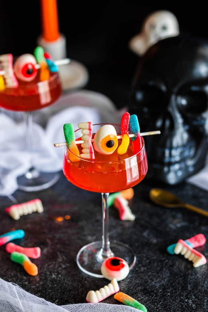 A coupe glass filled with Halloween punch and garnished with spooky gummy candies.