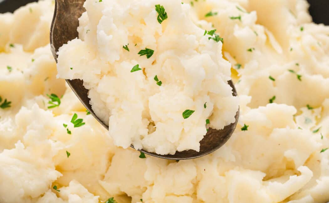 A bowl of a creamy mashed potatoes recipe with a spoon lifting some up.