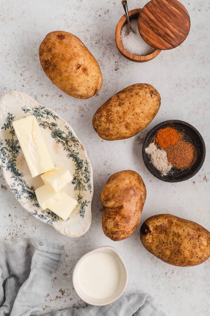 Ingredients laid out on a light surface including spuds, butter, seasoning and milk.