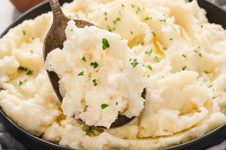 A bowl of russet mashed potatoes garnished with parsley.