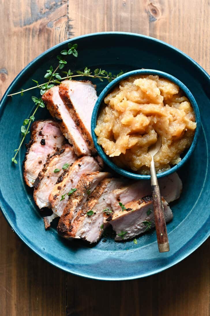 Shallow blue bowl filled with sliced pork chops and applesauce.