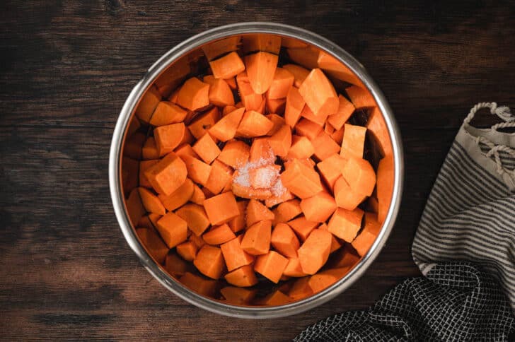 Cubed orange vegetables and salt in a metal bowl.