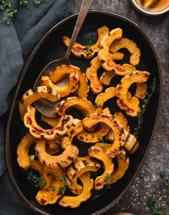 An oblong black platter topped with roasted delicata squash slices.