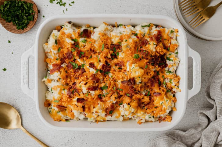 A white rectangle baking dish filled with a light colored casserole mixture topped with shredded cheese and bacon, after baking