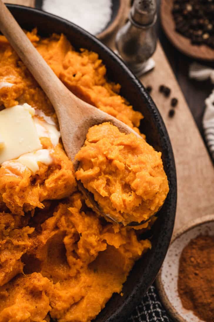 An instant pot sweet potato side dish in a black bowl with a wooden spoon.