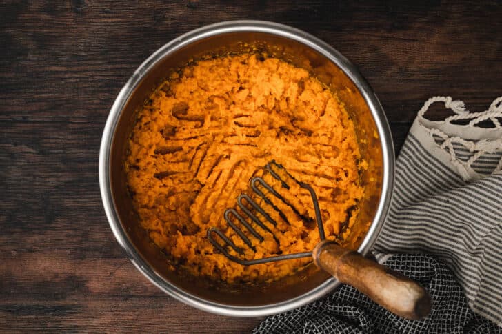 Sweet potatoes in instant pot bowl being mashed with a potato masher.