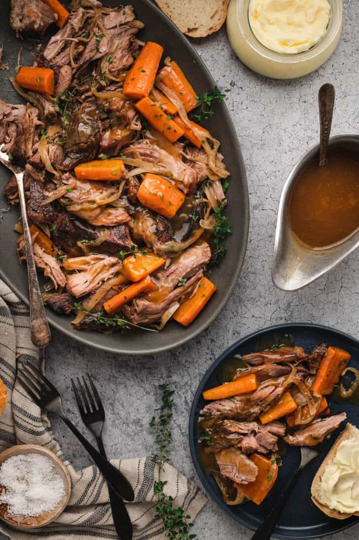 A platter and a plate of a pork roast crock pot recipe with onions, thyme and carrots.