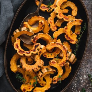 An oblong black platter topped with roasted delicata squash slices.