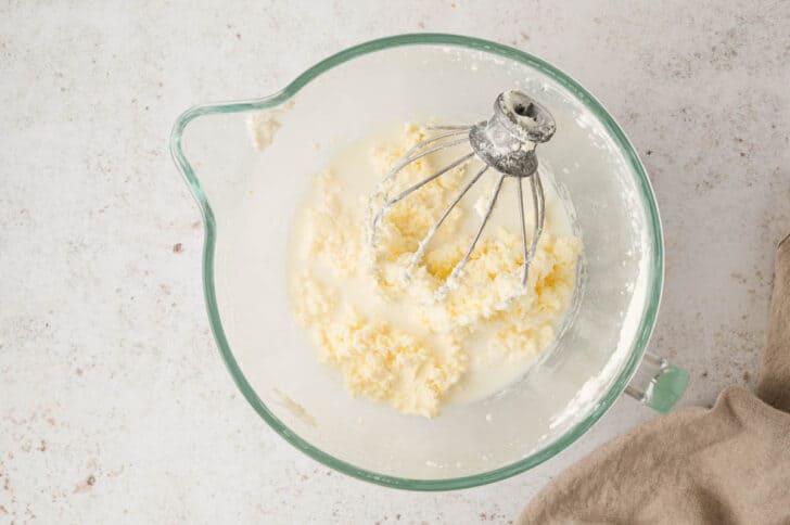 A glass stand mixer bowl filled with broken cream.
