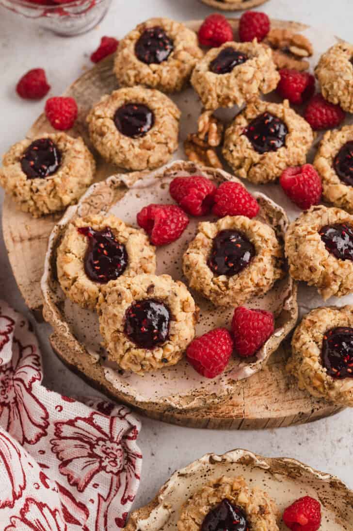 Raspberry thumbprint cookies on a small rustic plate and a larger wooden platter, with fresh raspberries.