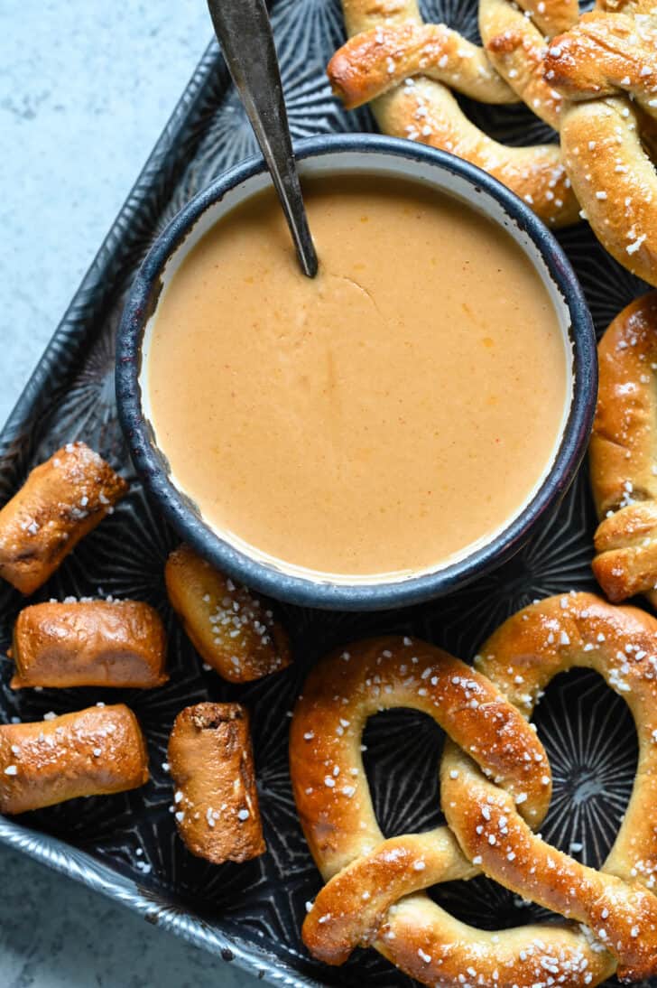 A bowl of easy beer cheese dip surrounded by soft pretzels.