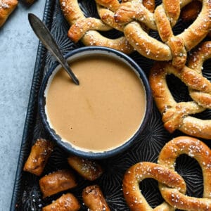 A bowl of beer cheese dip surrounded by soft pretzels.