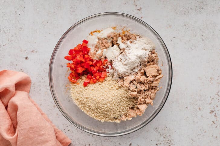 A glass bowl filled with canned fish, breadcrumbs, chopped red pepper and flour.