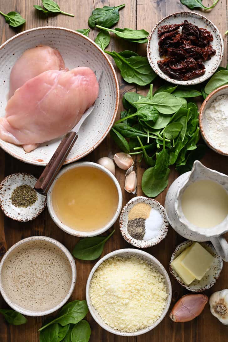 Ingredients on a wooden surface, including poultry, spices, spinach, cheese, garlic and shallots.