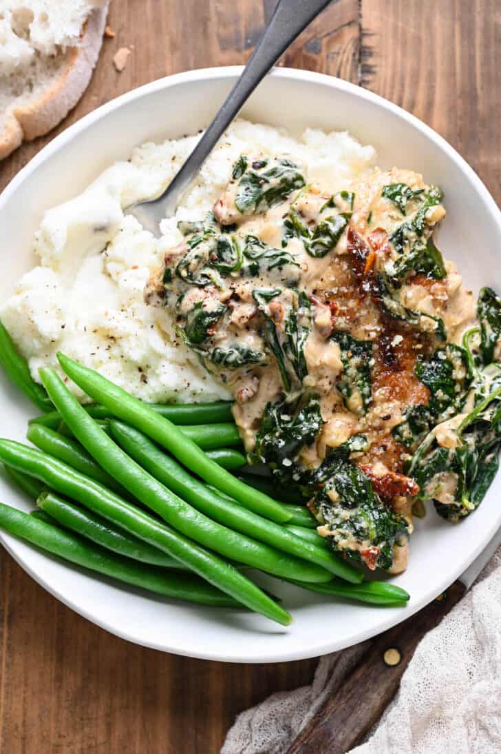 A white bowl filled with mashed potatoes, green beans and creamy chicken Florentine.