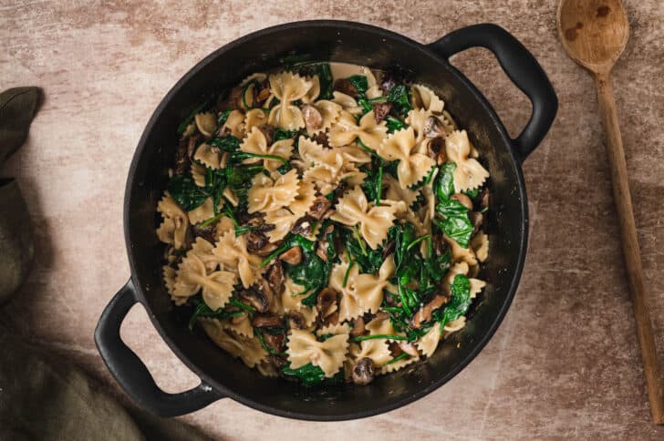 A dark dutch oven filled with creamy mushroom spinach pasta.