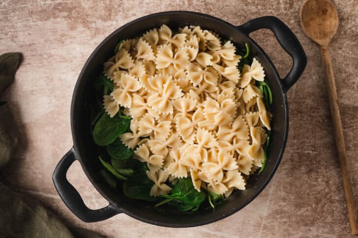 A dark dutch oven filled with spinach and farfalle noodles.