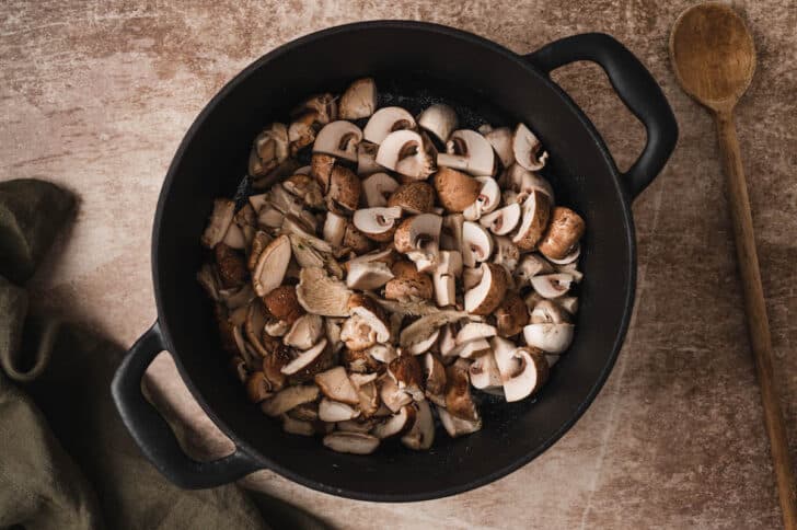 A dark dutch oven filled with chopped mushrooms.