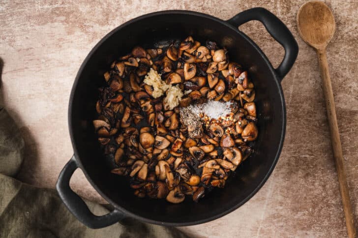 A dark dutch oven filled with cooked mushrooms and spices.