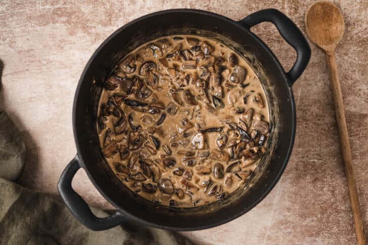 A dark dutch oven filled with a creamy mushroom sauce.