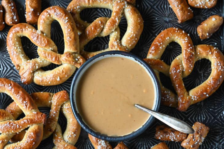A bowl of beer cheese dip surrounded by soft pretzels.
