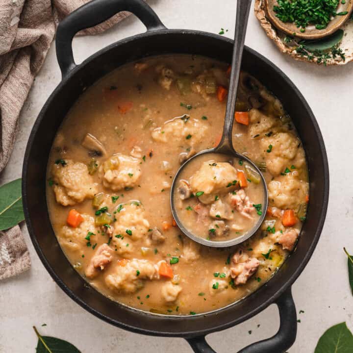 A black cast iron pot filled with chicken and dumplings, with a ladle lifting some out.