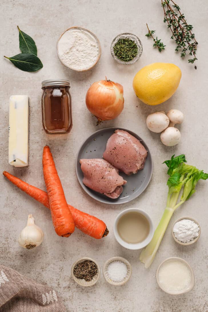 Ingredients laid out on a light surface, including poultry, mirepoix vegetables, mushrooms, herbs, butter, flour and spices.