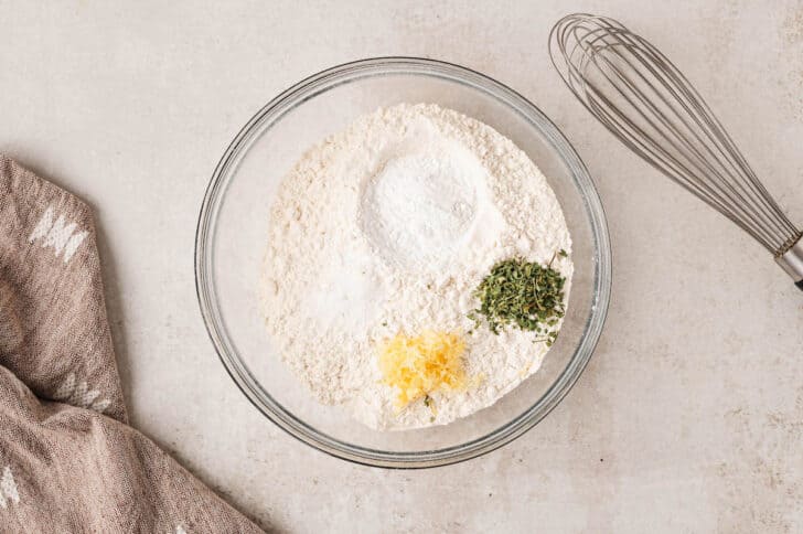 A glass bowl filled with flour, lemon zest and herbs.