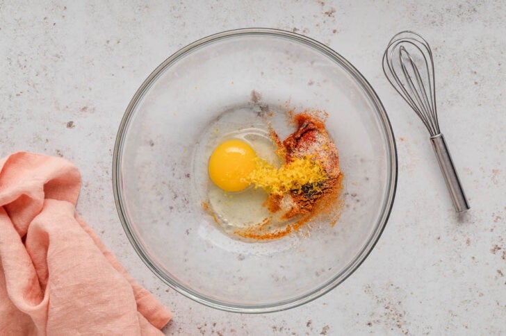 A glass bowl filled with an egg, lemon zest and spices.