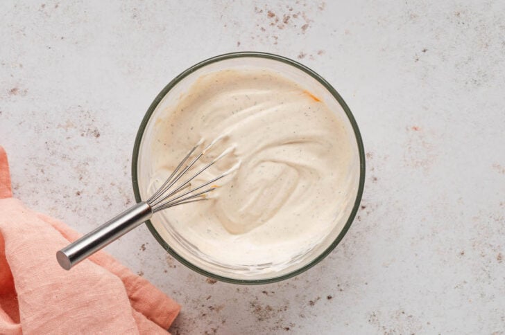 A glass bowl filled with a creamy sauce, with a whisk stirring it.