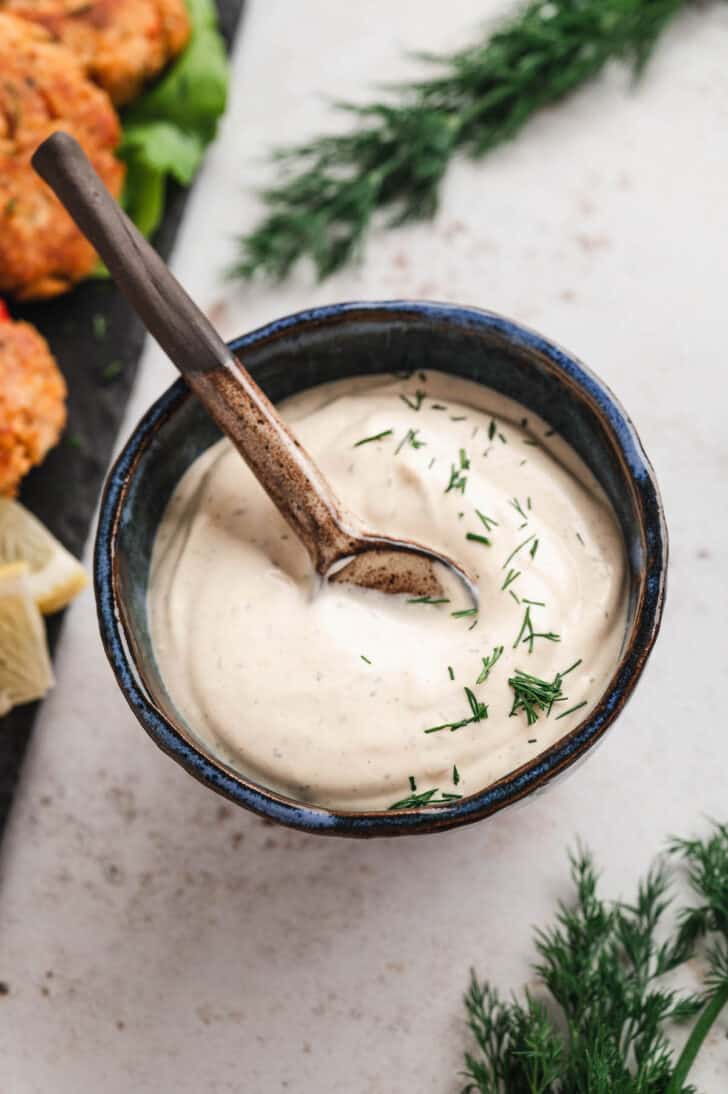 A bowl of dill sauce for salmon patties, with a spoon lifting some sauce out.