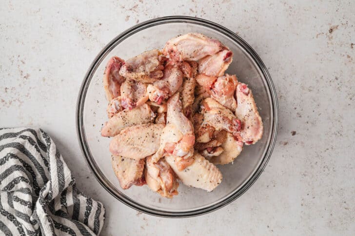 Glass bowl filled with poultry pieces seasoned with salt and pepper.