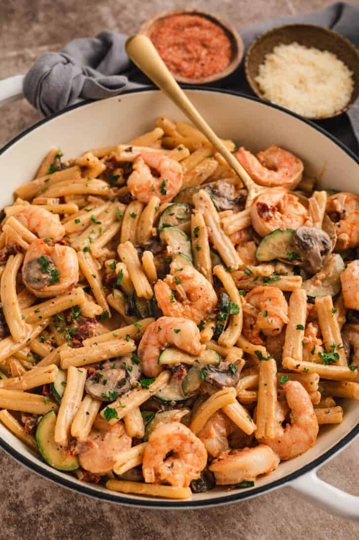 A white Dutch oven filled with Cajun shrimp pasta made with zucchini and mushrooms.