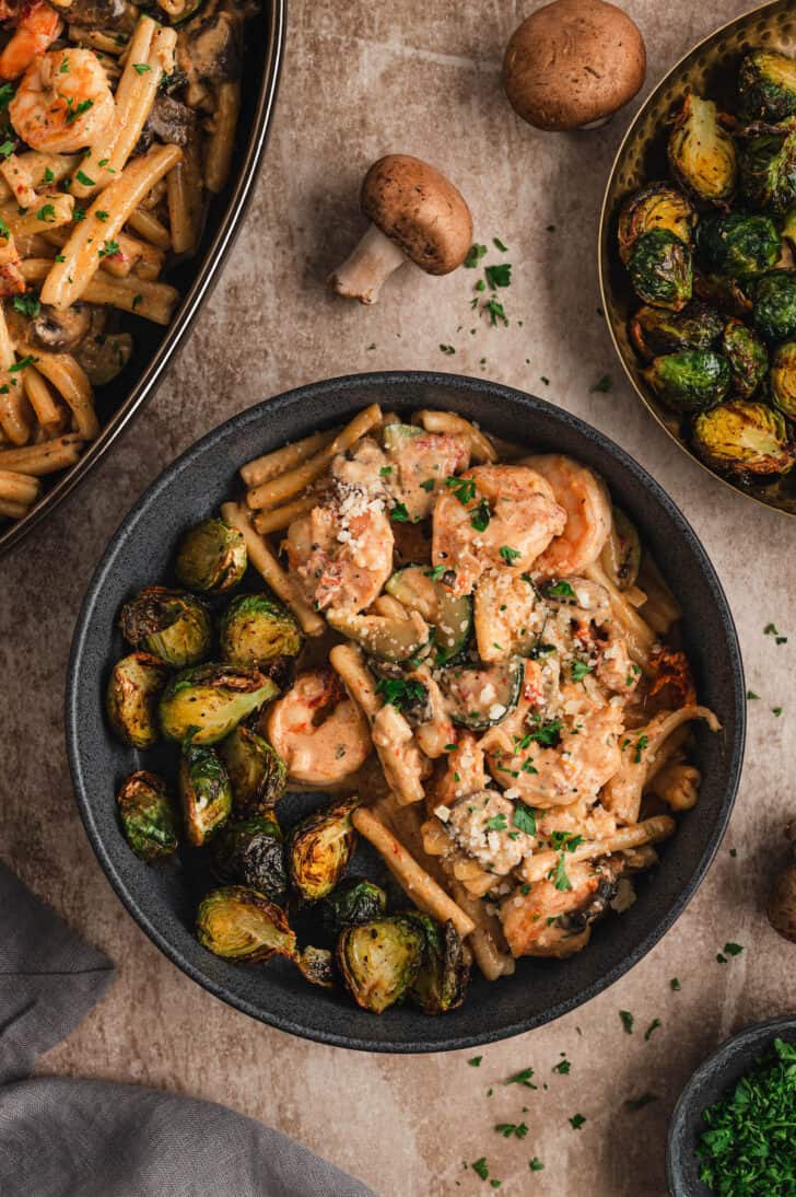 A dark bowl filled with creamy Cajun shrimp pasta and Brussels sprouts.