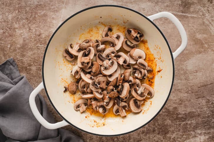 A white Dutch oven filled with mushrooms.