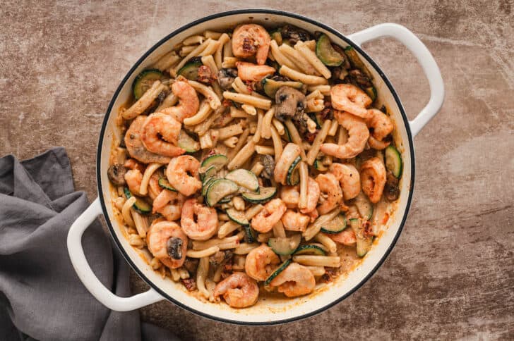 A white Dutch oven filled with a Cajun shrimp pasta recipe.