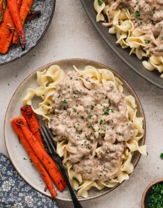 A ground beef stroganoff recipe plated over egg noodles with a side of roasted carrots.