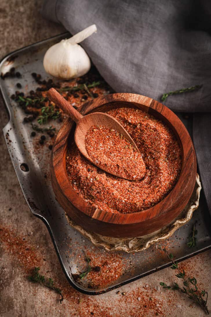 A wooden bowl filled with homemade Cajun seasoning, with a wooden scoop digging into it.
