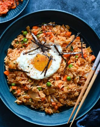 A blue bowl filled with kimchi fried rice, topped with a fried egg and sliced nori.