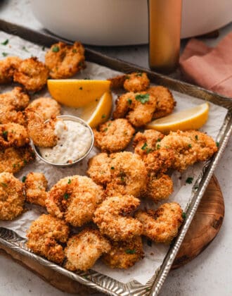 A rimmed baking pan full of air fryer popcorn shrimp resting in front of an air fryer.
