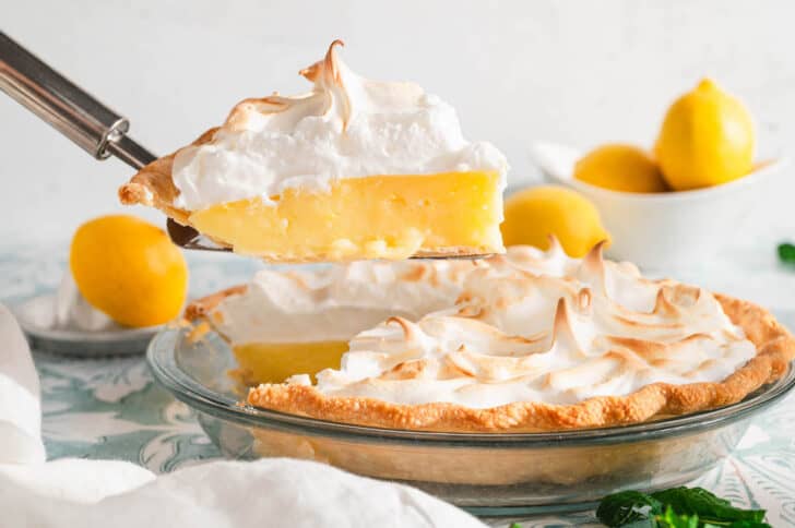 A piece of the best lemon meringue pie recipe being lifted from the pie in a glass plate.