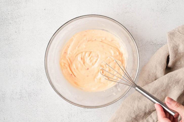 A whisk stirring a creamy orange sauce in a glass bowl.