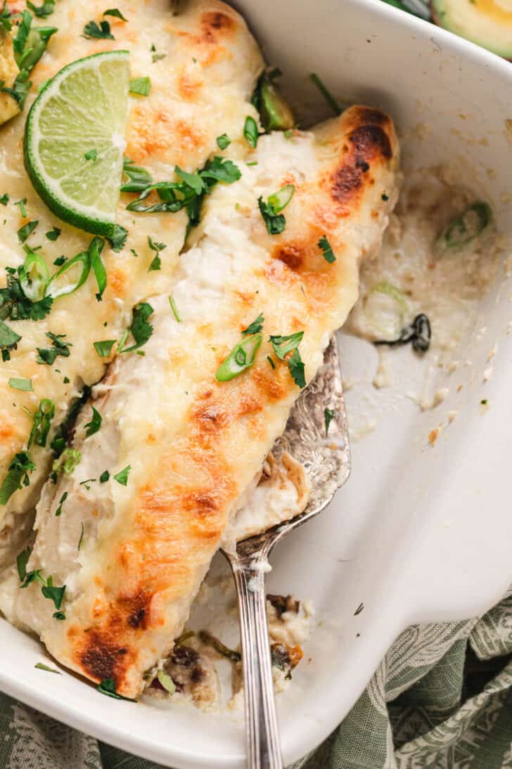 A white baking dish filled with vegetarian enchiladas recipe topped with green herbs and avocado.
